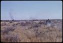 Expedition truck driving through a grassy field, showing smoke on horizon