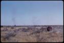 Expedition truck driving through a grassy field, showing smoke on horizon