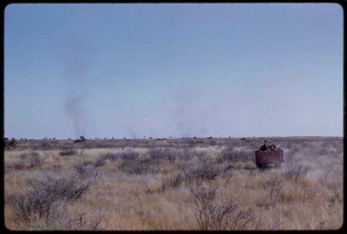 Expedition truck driving through a grassy field, showing smoke on horizon