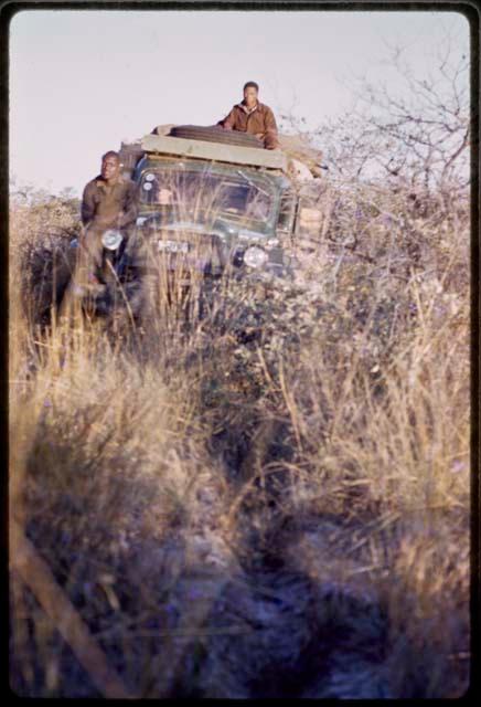 /Gishay and Simon Molamo on top of expedition truck driving through thick brush