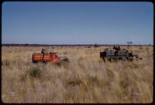 Expedition red Dodge and GMC driving through a grass field