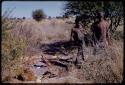 Oukwane and Gai standing to the side of a pile of bows and arrows