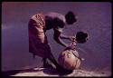 Woman with scarification on her back, filling a large gourd with water