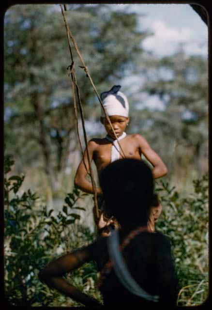 N!ai swinging on a naqm (swing), with another child watching her