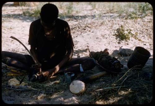 Man wearing a shirt, sitting under a tree, grinding something in a mortar