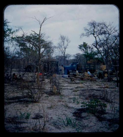 Expedition: Group of people, including expedition members, gathered near fire at the campsite in mangetti forest