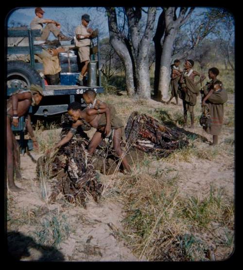 Expedition: Expedition members loading in a truck, with a man and a woman holding a baby on her back looking into baggage on the ground; other people watching the expedition members