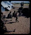 Expedition: Women and children sitting at the expedition camp, with a child with a lollipop walking in the center