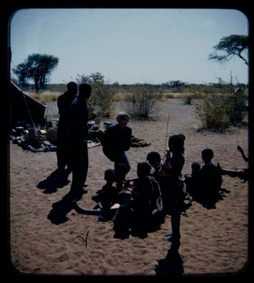 Expedition:  Lorna Marshall and two expedition members interacting with a group of women and children sitting at the expedition camp