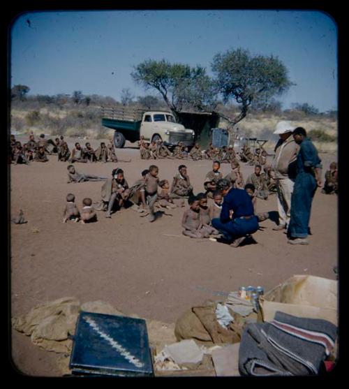 Expedition: Lorna Marshall talking to children, with Laurence Marshall and  Kernel Ledimo standing nearby and a group of people watching them in the background