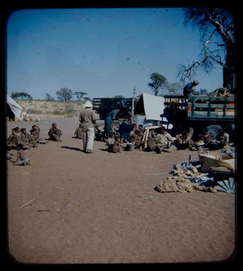 Expedition: Lorna Marshall and Kernel Ledimo probably getting gifts ready, with Laurence Marshall standing behind them and a group of people sitting nearby