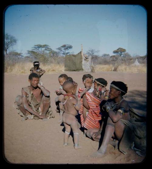 Expedition: Man and a woman sitting with a group of children; one is wrapped in striped cloth