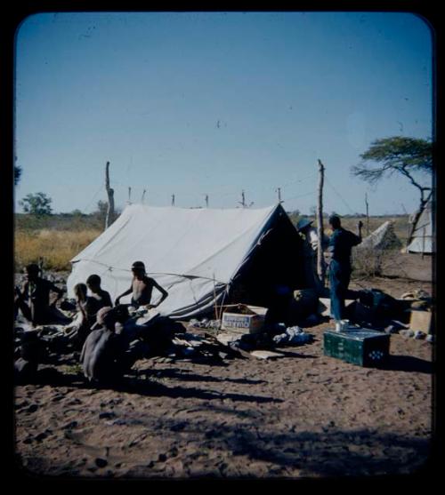 Expedition: Laurence Marshall and Kernel Ledimo standing in front of a tent, with a group of people sitting with gifts nearby