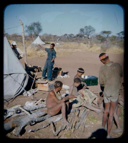 Expedition: Group of people sitting by a tent, with Lorna Marshall and Kernel Ledimo standing in front of a tent in the background