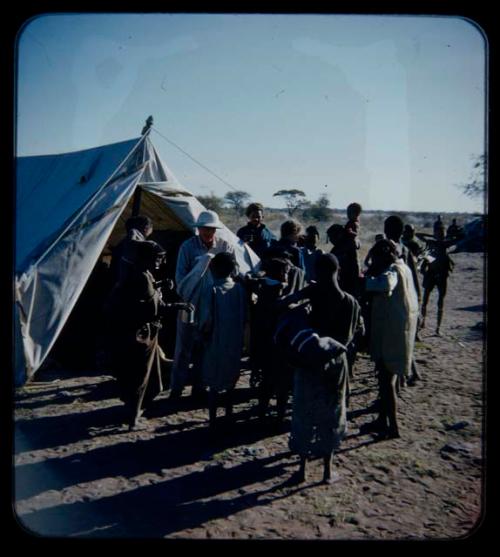 Expedition: Laurence Marshall and Lorna Marshall probably handing out gifts to a group of people in front of a tent