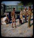 Expedition: Group of men, including ≠Toma, standing and a child sitting by a truck; John Marshall and another expedition member repairing something nearby