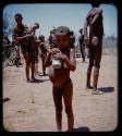 Expedition: Boy standing and holding a tin can in his hands, with other people in the background