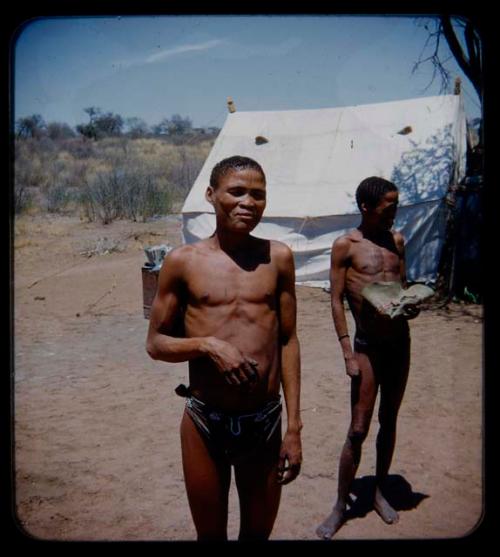 Expedition: Two men standing, with a tent in the background; one is holding a hat