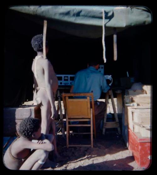 Expedition: Expedition member sitting and using sound recording equipment, with two boys watching them