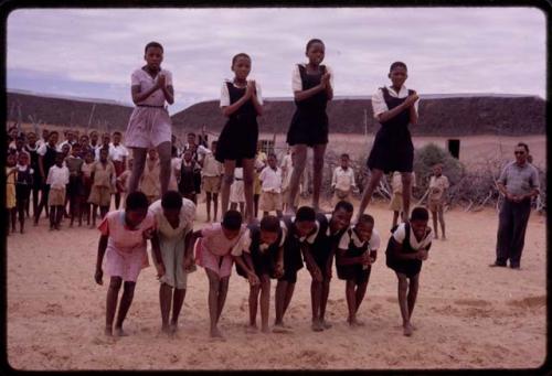 Girls standing on the backs of others, imitating horses, playing a game at recess at a school