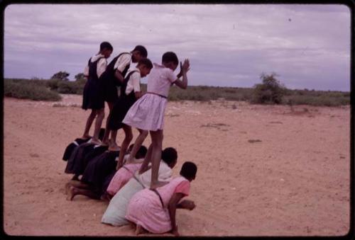 Girls standing on the backs of others, imitating horses, playing a game at recess at a school