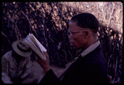 Preacher standing and holding a book, with a person sitting in the background