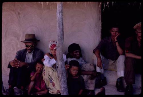 Leader of a group from Johannesburg (wearing hat) sitting with a group of people on a porch, including his son (in the doorway)