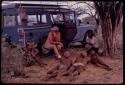 Group of young men sitting and lying down next to the expedition Land Rover, being interviewed by Nicholas England