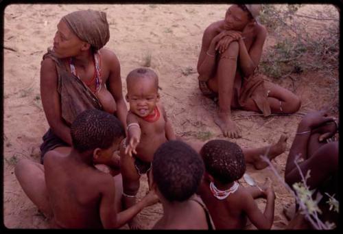 Group of women and children sitting, including a child wearing red beads