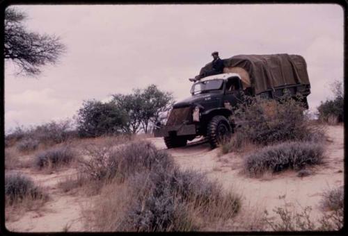 Expedition member sitting on the top of an expedition truck (Power Wagon) being driven down a sand dune