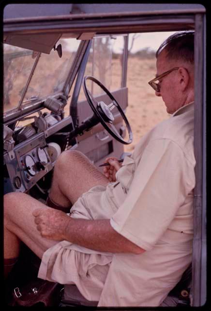 C. J. Mathias sitting in an expedition truck, writing a word game on his leg