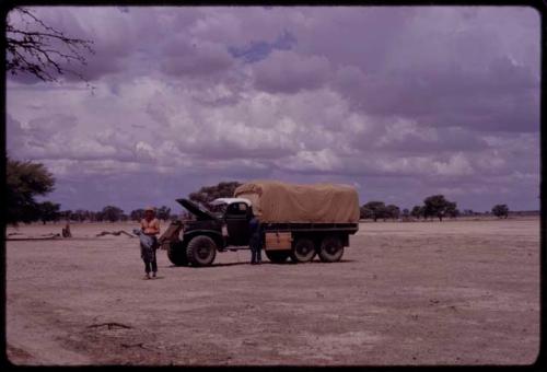 Kurt Ahrens and another expedition member standing next to one of the trucks covered with canvas for rain protection