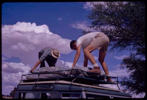 Kurt Ahrens helping Nicholas England to arrange his bed on the top of the expedition Land Rover