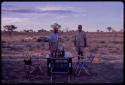 O. P. M. Prozesky and C. J. Mathias standing next to a table in the expedition camp, with blankets drying on bushes in the background