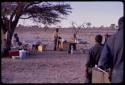 Philip Hameva standing in the kitchen area of the expedition camp, with other expedition members sitting near him