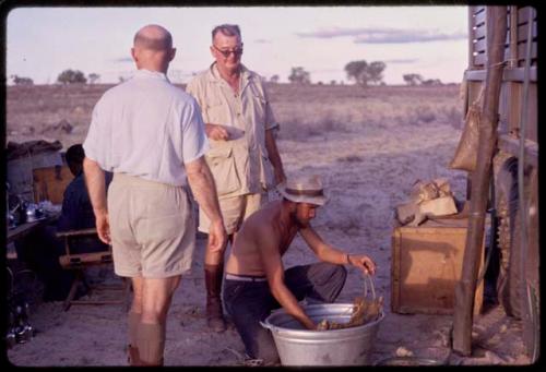 Kurt Ahrens filling water bags, with O. P. M. Prozesky and C. J. Mathias standing next to him