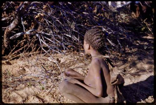 Boy sitting in sand, seen from behind