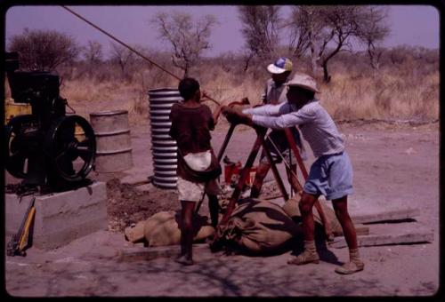 Group of people building a water pump; ǂToma and /Gao pulling on a rope