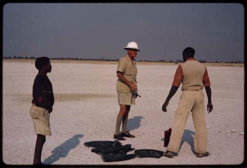 Claude McIntyre with two men deciding on direction of wind, placing old tires to burn for a smoke signal for a plane