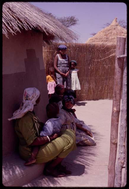 Kernel Ledimo's wife and some girls seated in shade by Kernel Ledimo's house