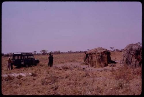 Huts with the expedition Land Rover parked and expedition members standing by