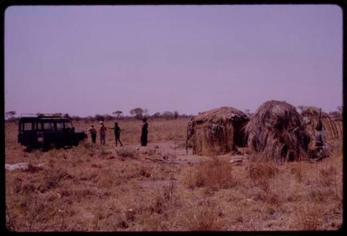 ǂToma's huts with the expedition Land Rover parked outside and expedition members standing by