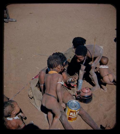 Expedition: Woman looking in a mirror, with two children watching, tin can and teapot on the ground next to them