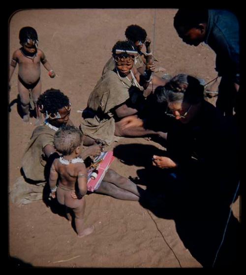 Expedition: Group of people sitting with Lorna Marshall, receiving gifts from her, with Kernel Ledimo leaning over them