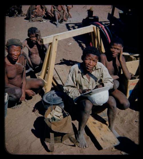 Expedition: ≠Toma wearing a shirt, holding a pith helmet, sitting with a group of people