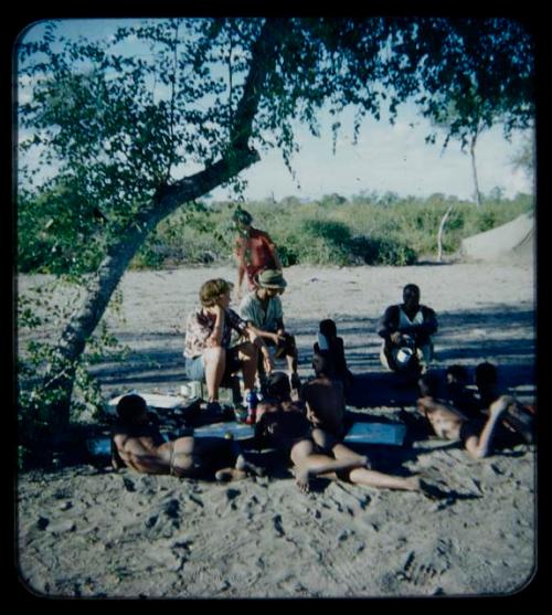 Expedition: Group of children lying with drawings on the ground, with expedition members including Elizabeth Marshall Thomas, Lorna Marshall, and Ngani sitting in the background