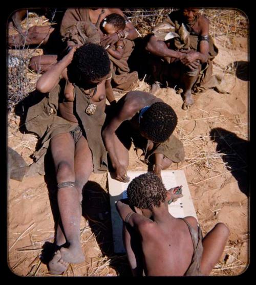 Expedition: Woman watching two children drawing with crayons next to her, and other people sitting in the background