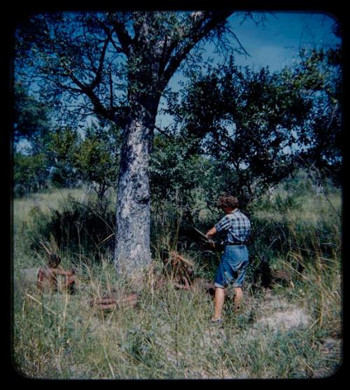 Expedition: Elizabeth Marshall Thomas standing with notebooks among trees, with people sitting in grass nearby