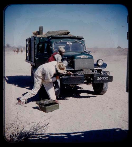 Expedition: Two men working on truck tracks, with horsemen and cattle in the background