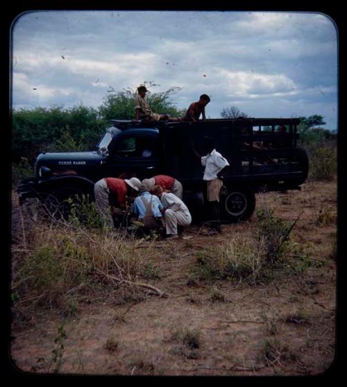 Expedition: John Marshall, Ngani, and other expedition members gathered around a water can, with an expedition truck and other men in the background, on their trip from "Kubi"